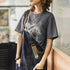 Person wearing a gray t-shirt with a graphic design, standing indoors.